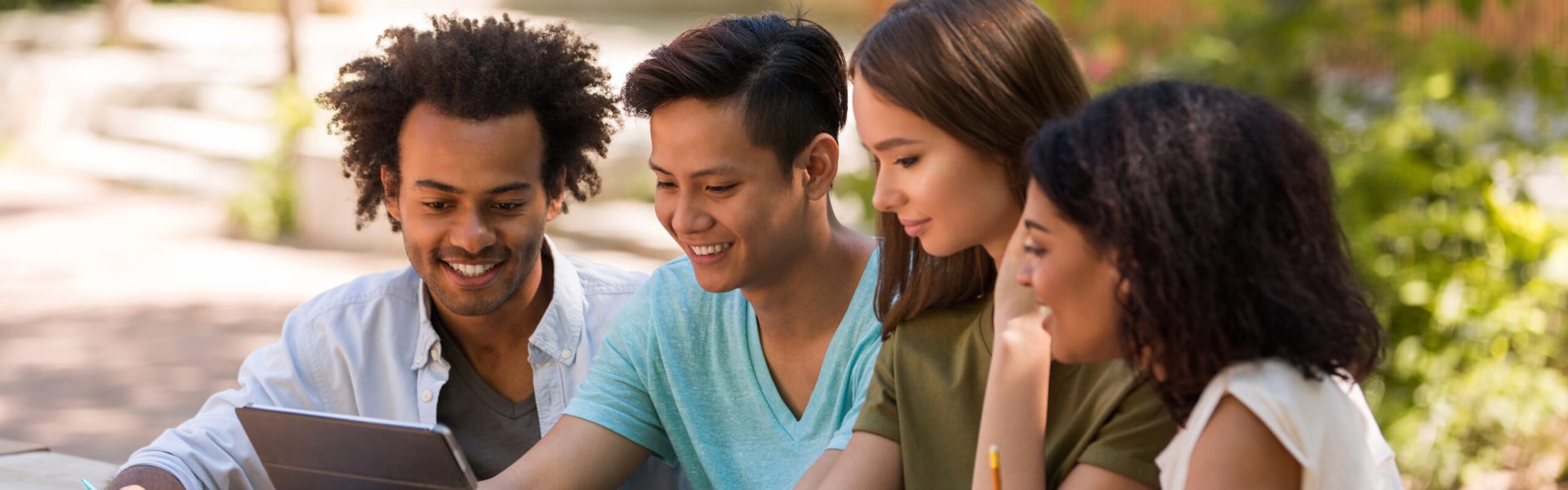 Photographie de 4 étudiants souriants (2 hommes et 2 femmes) travaillant en extérieur sur une tablette